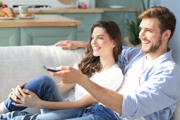 Joven pareja amorosa en el sofá de casa viendo la televisión y riendo.