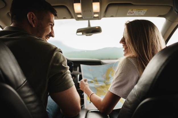 Joven pareja amorosa en un viaje por carretera con mapa dentro de un coche