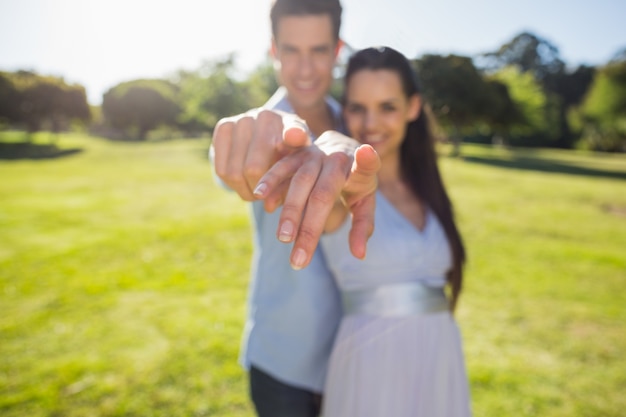 Joven pareja apuntando el dedo a la cámara en el parque