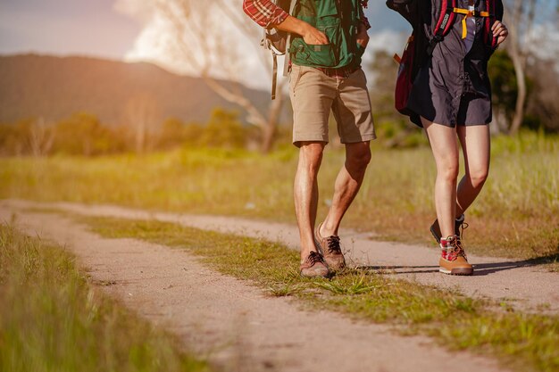 Joven pareja asiática en un amplio campo está caminando a pie para explorar el bosque como una actividad de vacaciones en la temporada de otoño del camino forestal. Senderismo, excursionista, equipo, bosque, camping, concepto de actividad.