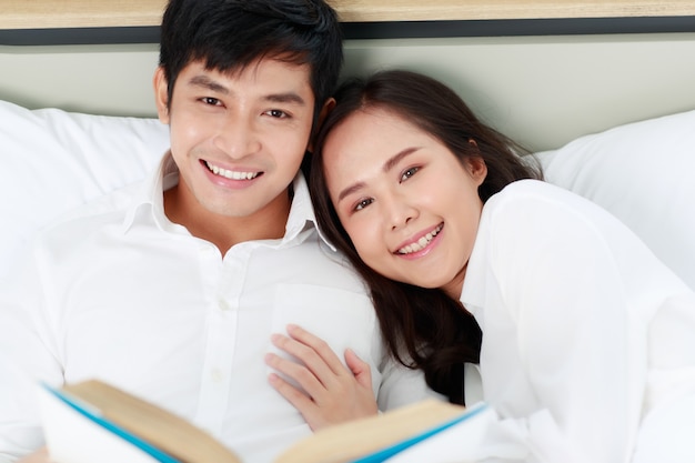 Joven pareja asiática atractiva feliz acostado juntos en la cama leyendo el libro