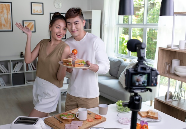 Joven pareja asiática blogger influencer vlogger grabando video en la cocina Un joven y una joven transmiten en vivo una clase de cocina desde casa