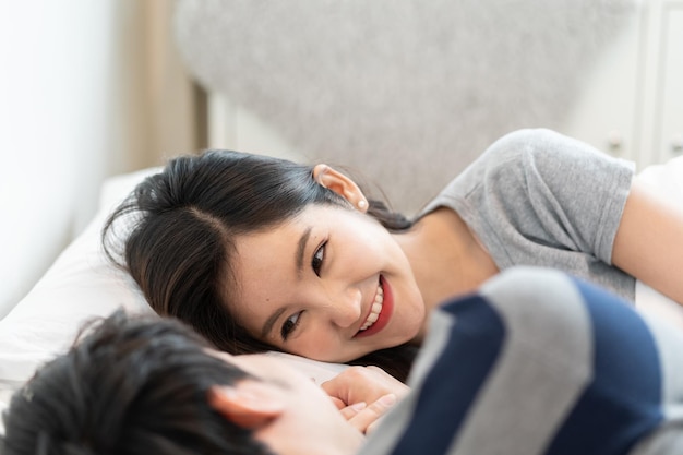 Joven pareja asiática en la cama en el dormitorio abraza y disfruta de la vida juntos y sonriendo por la mañana con felicidad