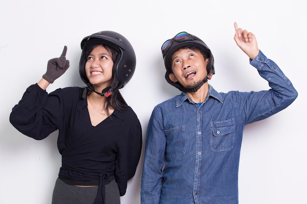Joven pareja asiática con un casco de motocicleta apuntando con los dedos en diferentes direcciones en blanco