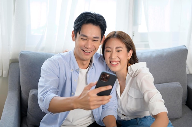 Joven pareja asiática sonriente usando un teléfono inteligente en la sala de estar en casa