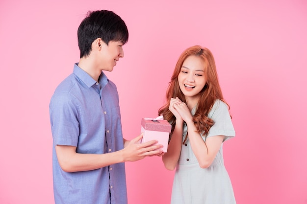 Joven pareja asiática sosteniendo una caja de regalo rosa sobre fondo rosa