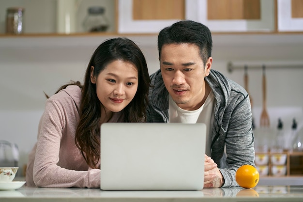 Una joven pareja asiática usando una computadora portátil juntos en casa.