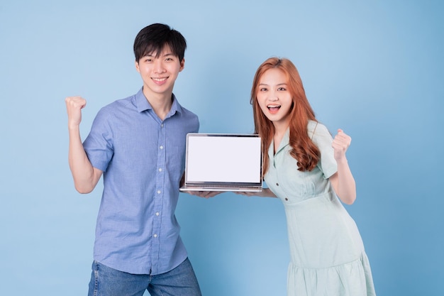 Joven pareja asiática usando laptop sobre fondo azul.