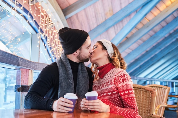 Joven pareja atractiva en una cita en un café, hablando y besándose en Navidad