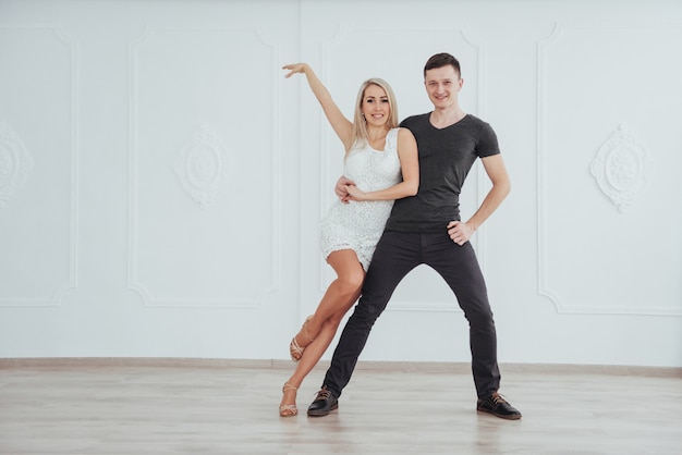 Joven pareja bailando música latina: bachata, merengue, salsa. Dos elegancia posan en sala blanca