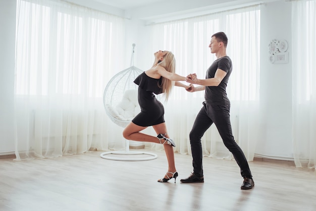 Joven pareja bailando música latina: bachata, merengue, salsa. dos elegancia posan en sala blanca