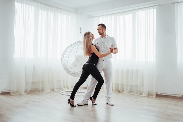 Joven pareja bailando música latina: bachata, merengue, salsa. Dos elegancia posan en sala blanca