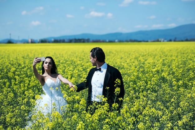 Joven pareja de bodas de chica sexy con cara bonita en vestido de novia blanco tiene teléfono móvil y manos