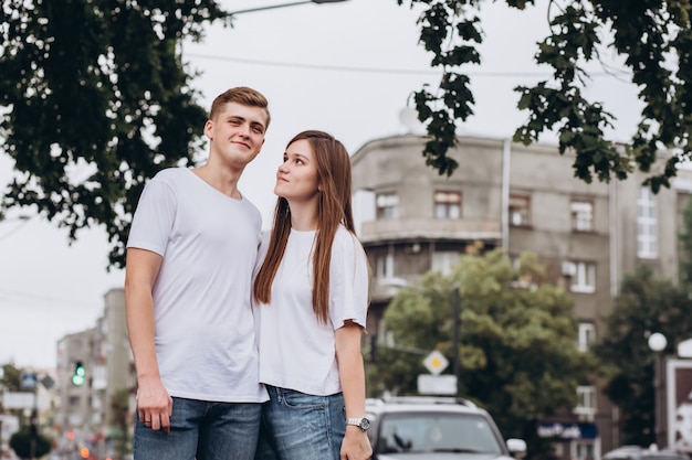 Joven pareja con camisetas blancas y jeans camina por las calles de la ciudad y se dan la mano.