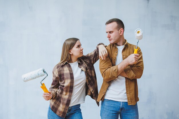 Una joven pareja casada enamorada pinta las paredes con pintura blanca usando rodillos Renovación en el apartamento de una pareja feliz