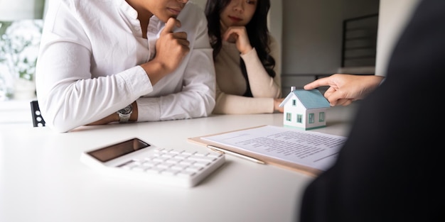 Foto una joven pareja casada sentada a la mesa escuchando a un agente inmobiliario, un agente de préstamos o un asesor hipotecario hablar sobre las opciones