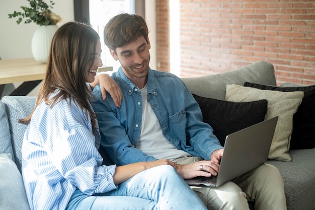 Una joven pareja casada sentada en el sofá en la sala de estar de su casa usando una tableta PC para Internet y redes sociales Una familia feliz descansando en el sofa disfrutando del fin de semana viendo video o hablando en video llamada