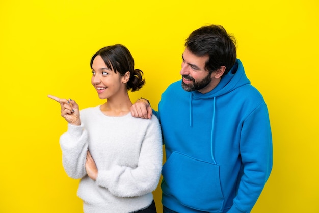 Foto joven pareja caucásica aislada de fondo amarillo apuntando hacia un lado para presentar un producto
