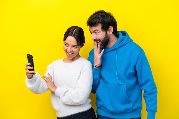 Joven pareja caucásica aislada de fondo amarillo haciendo un selfie con el móvil
