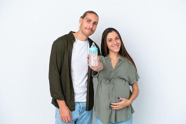 Joven pareja caucásica aislada de fondo blanco embarazada y sosteniendo un biberón