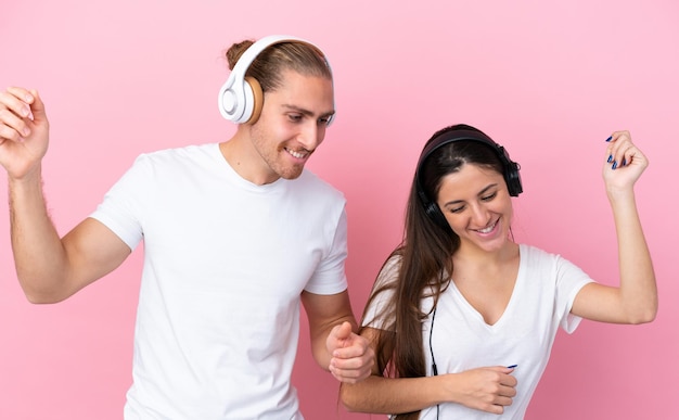 Joven pareja caucásica aislada de fondo rosa escuchando música y bailando