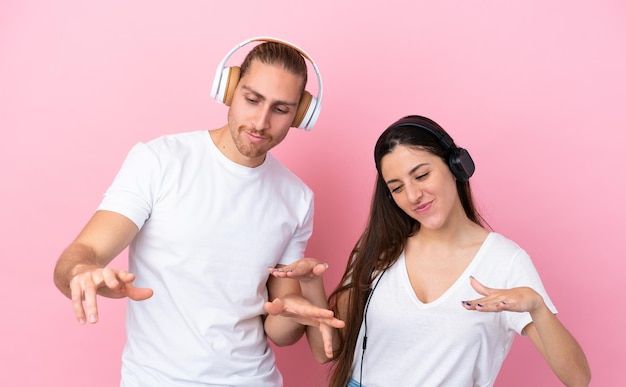 Joven pareja caucásica aislada de fondo rosa escuchando música y bailando