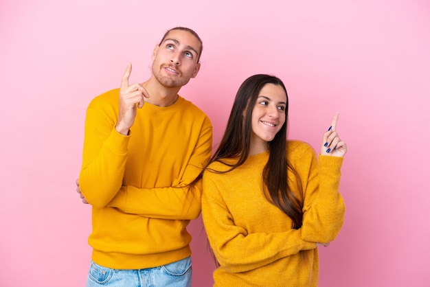 Joven pareja caucásica aislada de fondo rosa señalando una gran idea y mirando hacia arriba