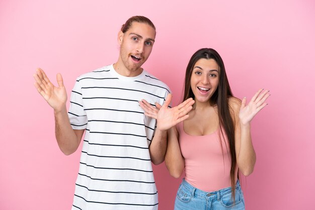 Joven pareja caucásica aislada de fondo rosa con sorpresa y expresión facial conmocionada