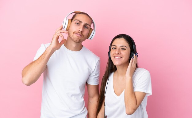 Joven pareja caucásica aislada sobre fondo rosa escuchando música