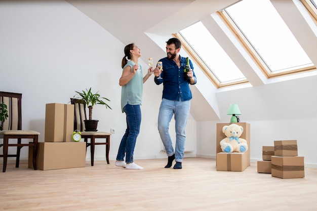 Joven pareja caucásica bailando y bebiendo champán para celebrar su primer día en el nuevo hogar.