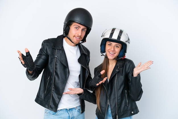 Una joven pareja caucásica con un casco de motocicleta aislado de fondo blanco con expresión facial sorprendida y sorprendida