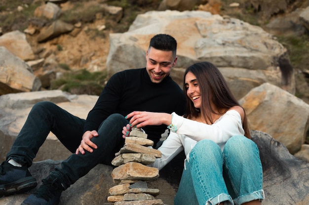 Joven pareja caucásica construyendo una torre de roca en la playa