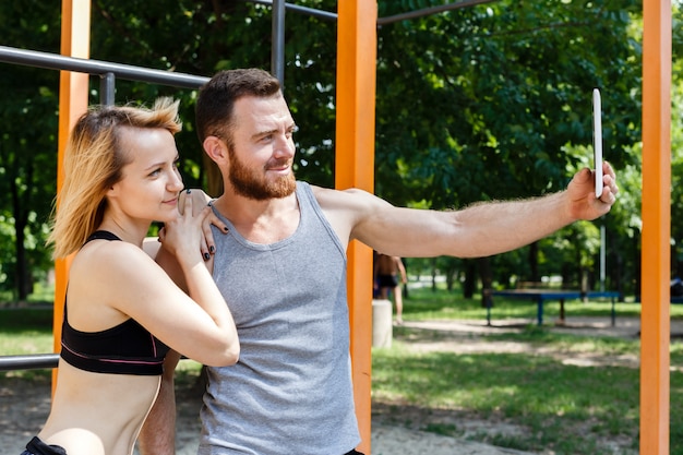 Joven pareja caucásica haciendo selfie foto mientras hace ejercicios de fitness en el parque.
