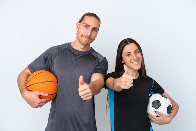 Joven pareja caucásica jugando baloncesto y fútbol aislada de fondo blanco dando un gesto de aprobación porque algo bueno ha sucedido