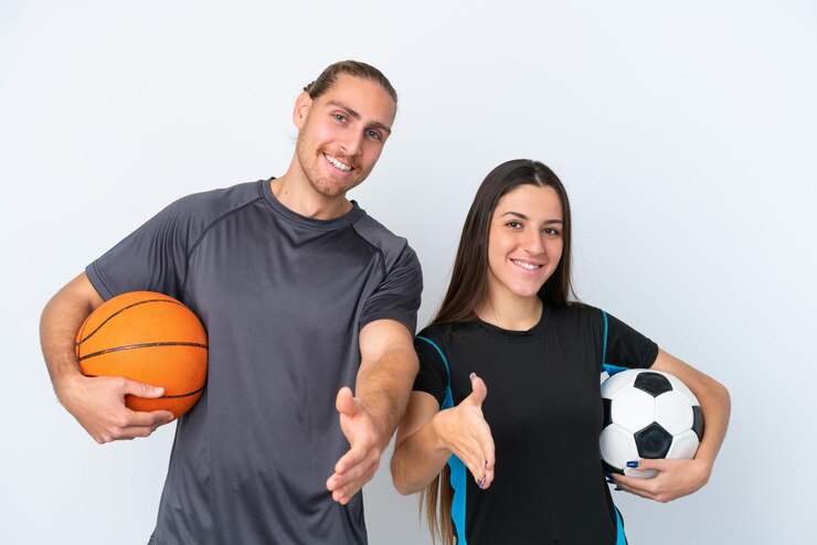 Foto una joven pareja caucásica jugando baloncesto y fútbol aislada de fondo blanco estrechando la mano para cerrar un buen trato