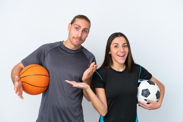 Una joven pareja caucásica jugando baloncesto y fútbol aislada de fondo blanco con expresión facial sorprendida y sorprendida