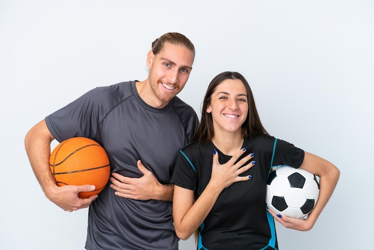 Foto una joven pareja caucásica jugando baloncesto y fútbol aislada de fondo blanco sonriendo mucho mientras se pone las manos en el pecho