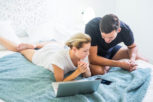 Joven pareja caucásica milenaria moderna trabaja en casa en el dormitorio con computadora portátil y teléfono y tecnología de internet en línea