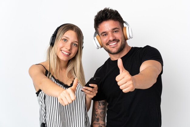 Joven pareja caucásica sobre fondo blanco escuchando música y con el pulgar hacia arriba