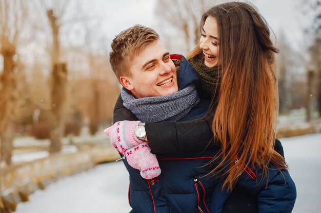 Una joven pareja en chaquetas de invierno y bufandas caminan en un parque cubierto de nieve