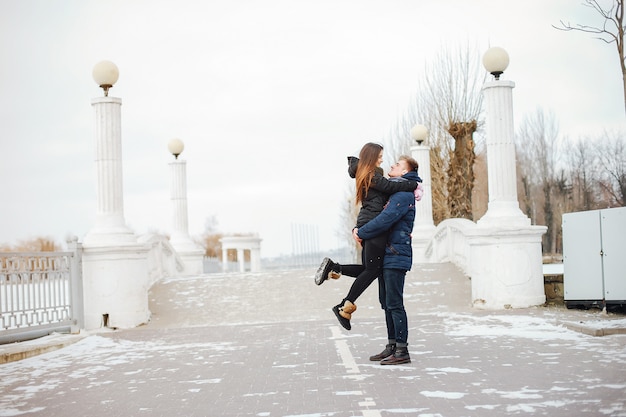 Una joven pareja en chaquetas de invierno y bufandas caminan en un parque cubierto de nieve