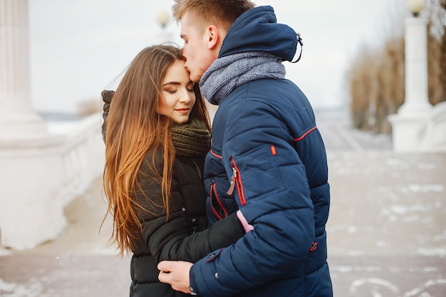 Una joven pareja en chaquetas de invierno y bufandas caminan en un parque cubierto de nieve