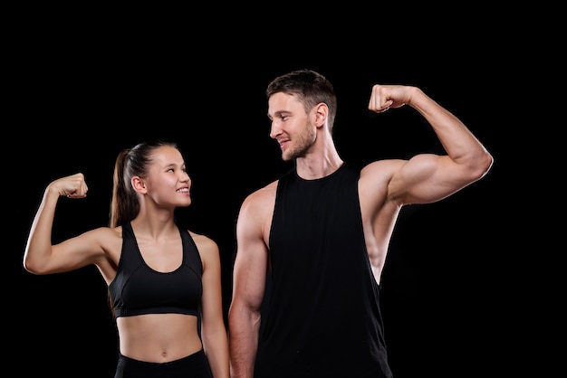 Joven pareja de deportes alegres en ropa deportiva mirando el uno al otro mientras muestra su fuerza