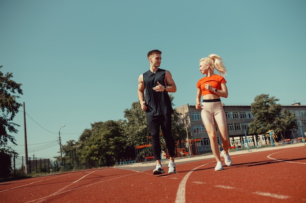 Joven pareja de deportes corriendo en el estadio en la pista de atletismo