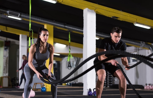 Joven pareja de deportes en forma trabajando en un gimnasio de entrenamiento funcional haciendo ejercicios de fitness cruzados con cuerdas de batalla