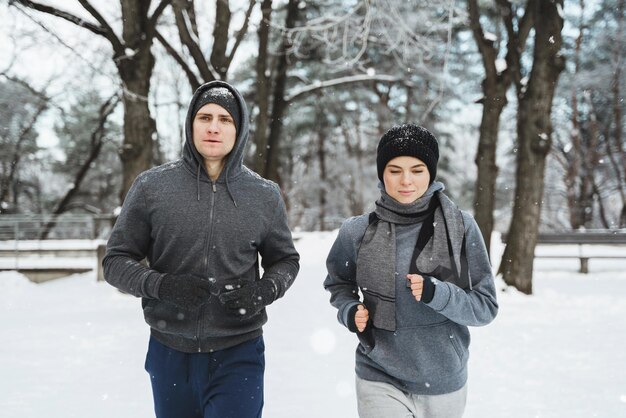 Joven pareja deportiva corre en el parque nevado durante el entrenamiento de jogging de invierno