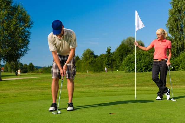 Joven pareja deportiva jugando al golf en un curso