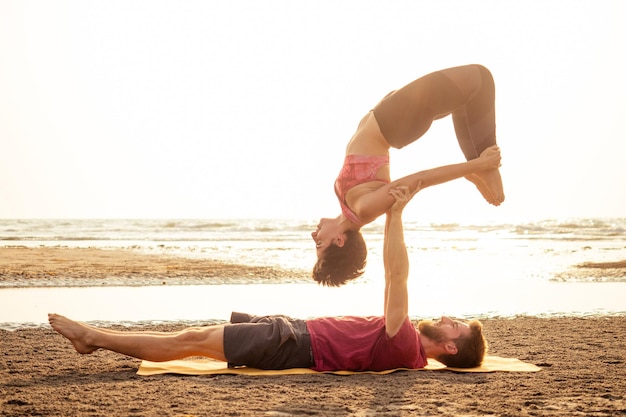 Una joven pareja deportiva, niña y niño, está practicando ejercicios de acroyoga al atardecer en la playa.