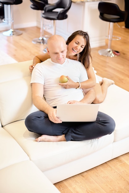 Una joven pareja descansando en el sofá con un ordenador portátil. Redes sociales. Concepto de amor, felicidad, gente y diversión. Concepto de familia, familia feliz