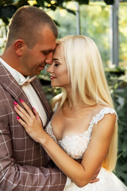 Joven pareja disfrutando de momentos románticos mientras camina en el parque. Elegante novia y el novio posando y besándose en el parque el día de su boda. Elegante novia en un hermoso vestido blanco, el novio en un traje.